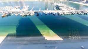 An aerial view of a marina with boats docked, a pier, and a beach with sun loungers. - Modern Beachfront 3BR Apt | Near Marina & JBR (Dubai)