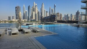 A poolside area with lounge chairs and a view of a city skyline. - Modern Beachfront 3BR Apt | Near Marina & JBR (Dubai)
