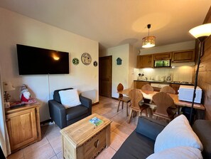 Ein Wohnzimmer mit Sofa, Couchtisch und Fernseher. Es gibt eine Küchenzeile mit Schränken und einer Mikrowelle.
