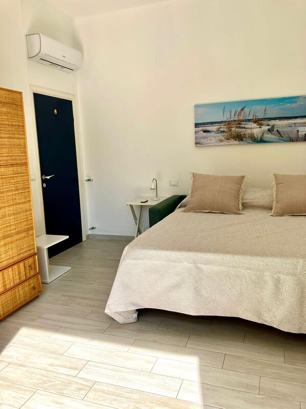 A bedroom with a bed, a nightstand, a lamp, a door, and an air conditioning unit.