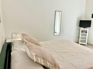 Een slaapkamer met een bed, een bedlamp, een tv-meubel en een spiegel.