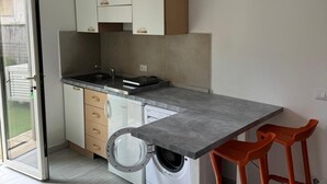 A compact kitchen with a built-in washing machine, a grey countertop, and two orange bar stools. - RAGGIO DI SOLE: STUDIO APARTMENT JUST A STONE'S THROW FROM THE BEACH (Castiglione della Pescaia)