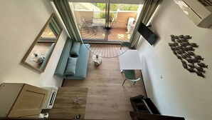 Et værelse med balkonudsigt, en sofa, et lille bord og et tv ophængt på væggen.