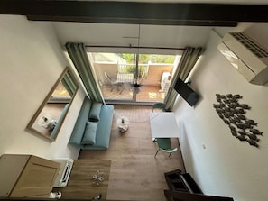 Ein Zimmer mit Balkonblick, einer Couch, einem kleinen Tisch und einem an der Wand befestigten Fernseher.