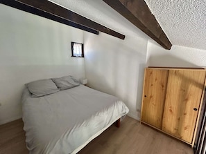 Ein Schlafzimmer mit einem Bett, einem Holzschrank und einem kleinen Fenster.