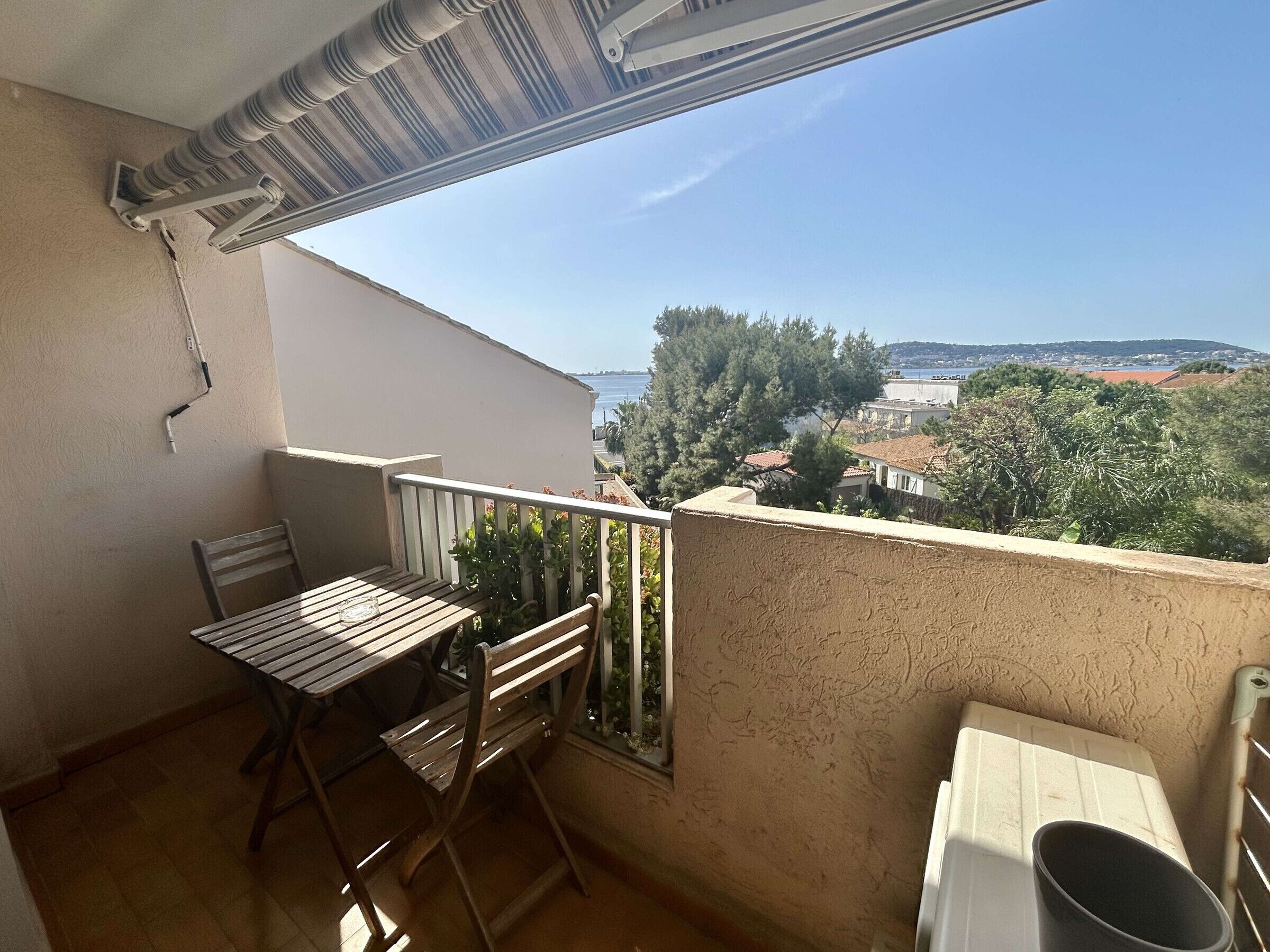 A balcony with a table and chairs, a window with a view of a coastal landscape, and a white radiator.