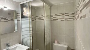 Et badeværelse med en glasbadeværelsesafskærmning, en hvid vask og et toilet.