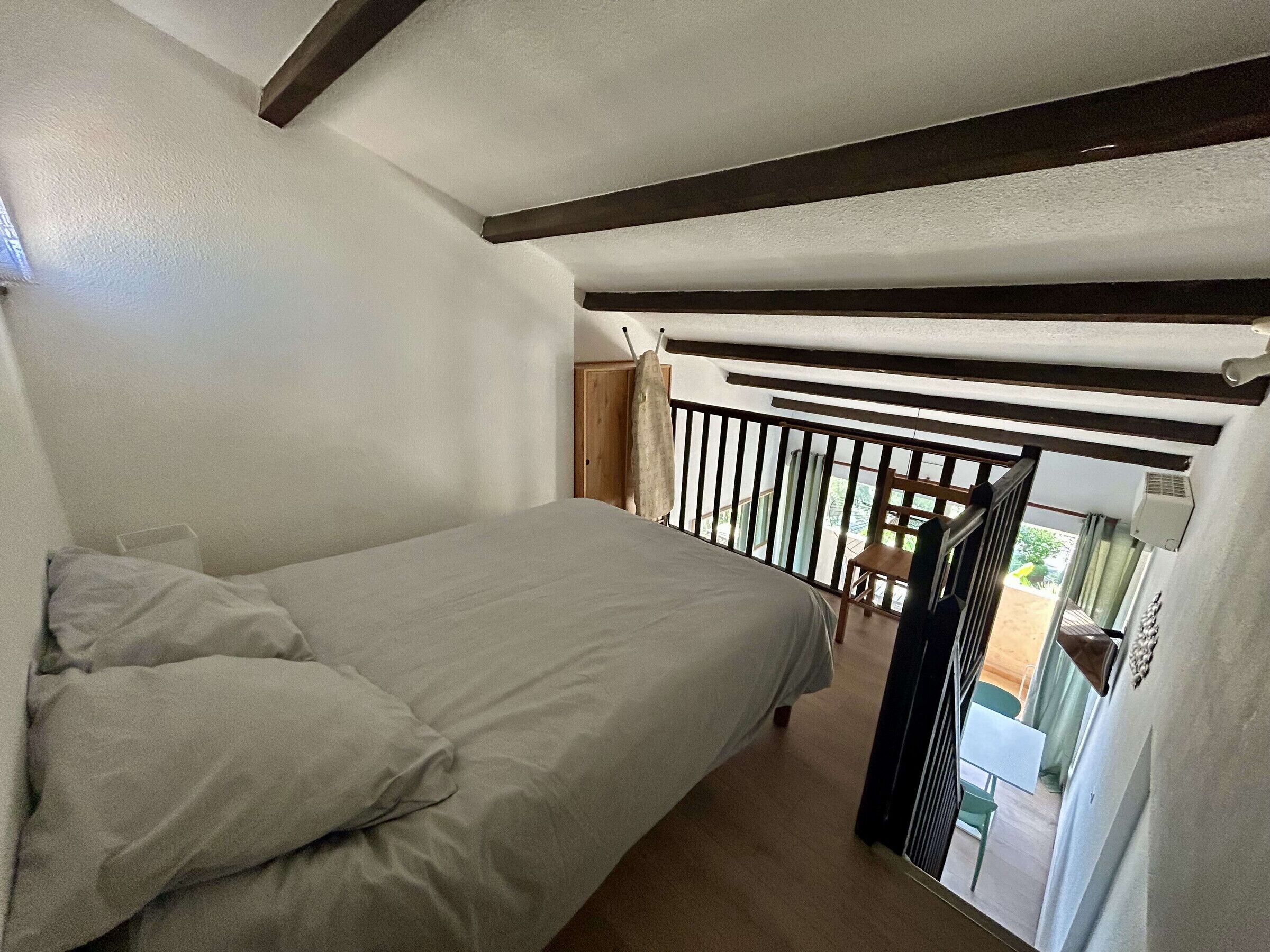 Quarto com uma cama, cabeceira de madeira, janela com vista e porta para uma varanda.