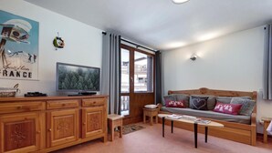 Ett mysigt vardagsrum med en soffa i trä, en tv-apparat placerad på ett träskåp och ett fönster med utsikt över en byggnad.