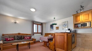 Ett mysigt vardagsrum med en soffa, ett soffbord och ett matbord. Ett kök med träskåp och en mikrovågsugn syns.
