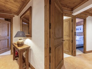 Un interior de madera con una lámpara sobre una mesa, un espejo y una puerta que da a otra habitación.