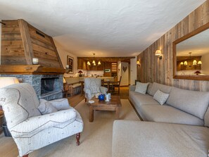 Ein gemütliches Wohnzimmer mit Kamin, einer Couch, einem Sessel und einem Essbereich im Hintergrund.