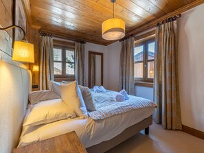 Eine Holzbalkendecke, ein Bett mit weißen Leinentüchern und ein Fenster mit Vorhängen.