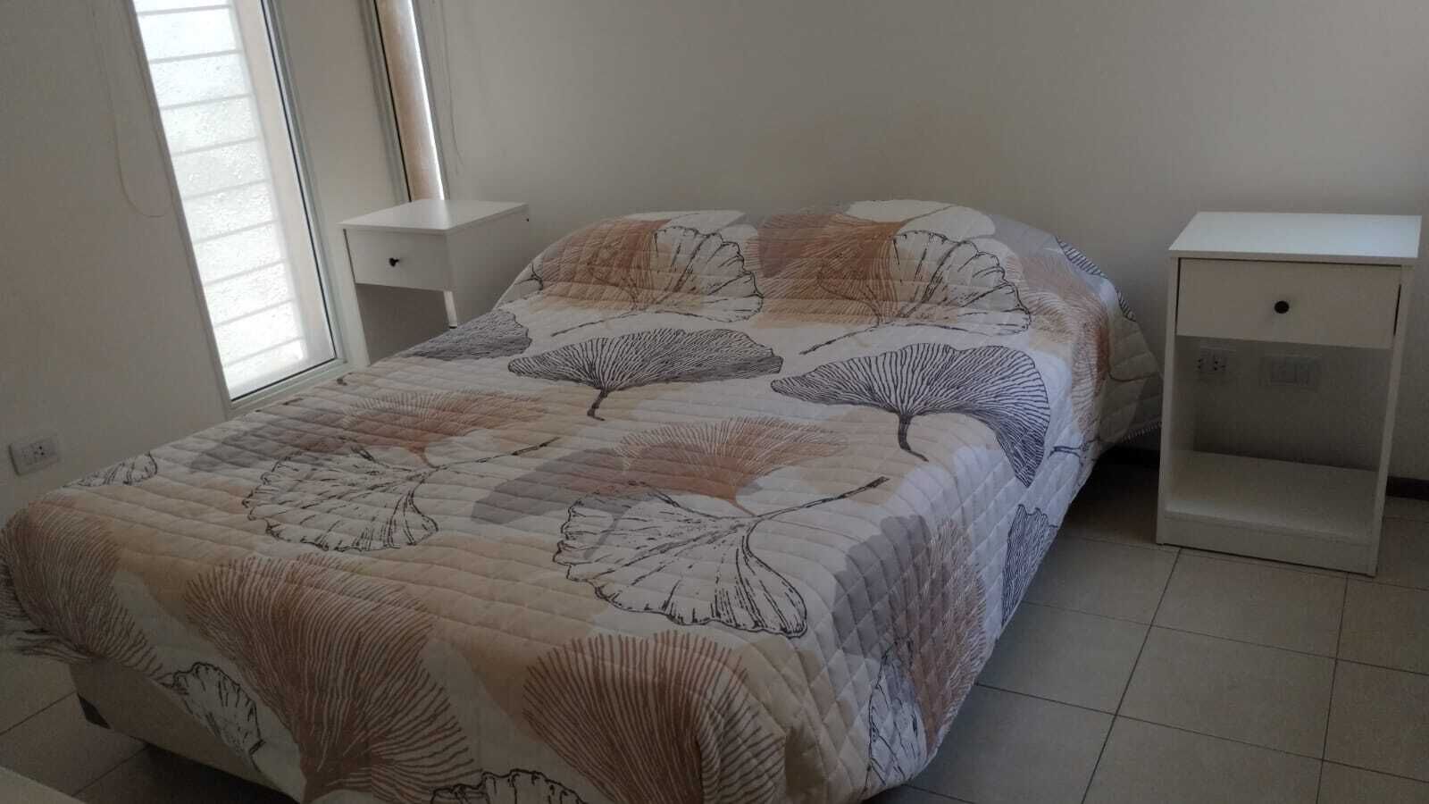 A bedroom with a bed, two nightstands, and a window with blinds.