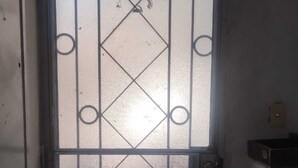 Um corredor estreito com porta de vidro jateado, com padrão de losangos e detalhes em metal decorativo.