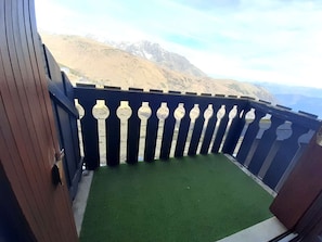 A balcony with artificial green turf, a dark blue railing with white balusters, and a mountainous backdrop.