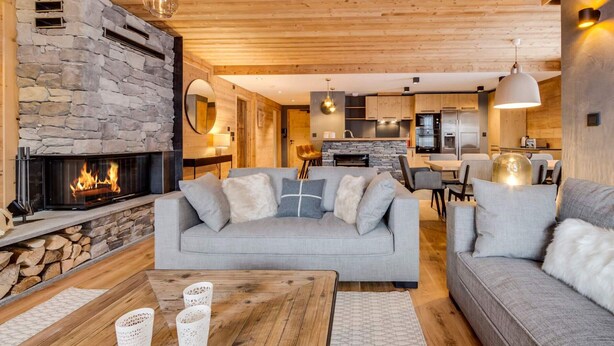 Ein gemütliches Wohnzimmer mit Kamin aus Stein, einem grauen Sofa und einem Holztisch.