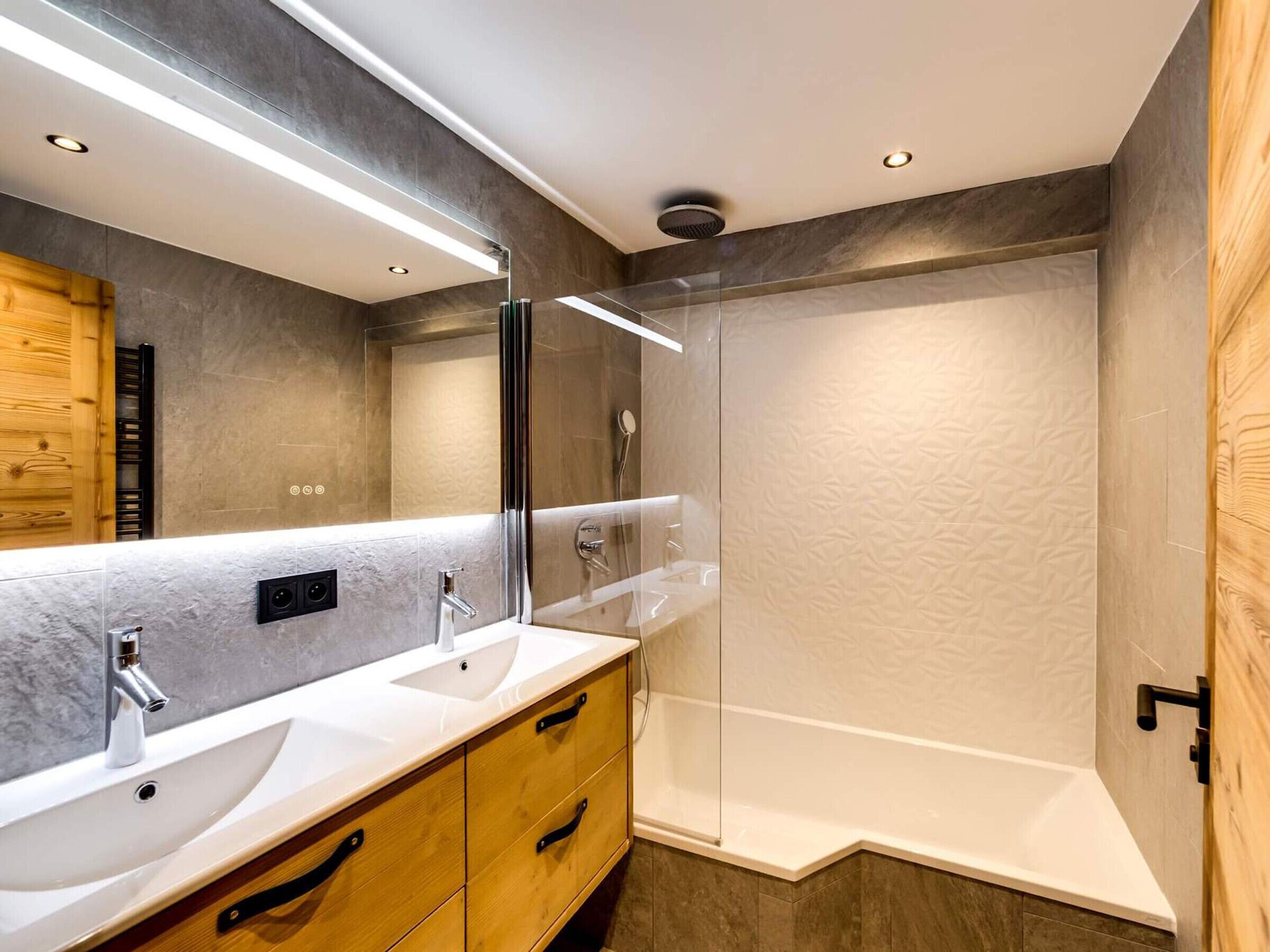 A modern bathroom with two sinks, a large mirror, and a glass-enclosed shower.
