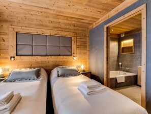 A wooden cabin room with two beds, a large padded headboard, bedside lamps, and a bathroom with a bathtub and a mirror. - Spacious apartment near slopes and shops - 8 guests (Val-d'Isère)