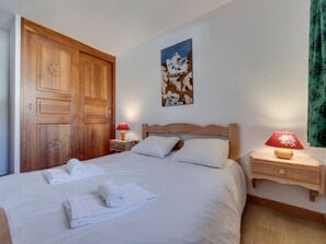Une chambre avec une porte en bois, un lit recouvert de draps blancs, deux tables de chevet avec des lampes et un tableau accroché au mur.