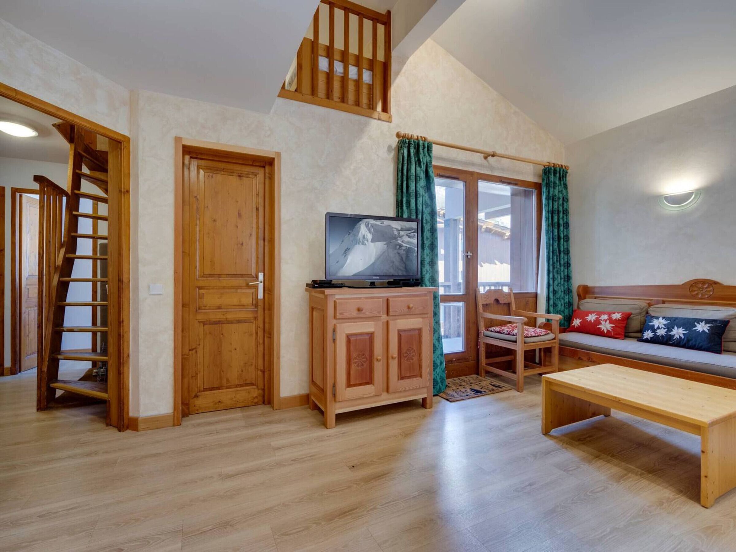 A cozy living room with a wooden staircase, a television on a cabinet, and a sofa with cushions.