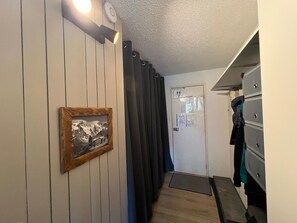 Ein schmaler Flur mit einer Holztür, einem gerahmten Bild an der Wand, einem schwarzen Vorhang und einer Bank.