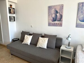 A grey sofa with white and grey cushions, a white side table with a lamp, and two framed artworks on the wall. - Casa Ángeles - Terraza y vista al mar (Torremolinos)