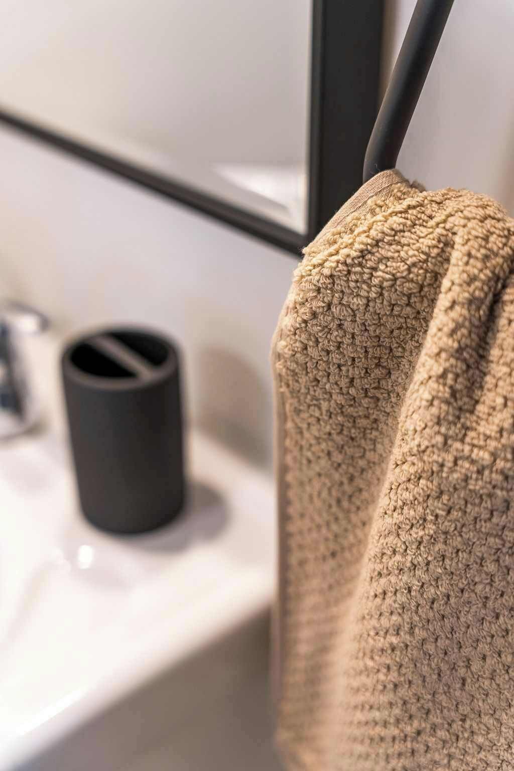 A bathroom with a towel hanging on a rack, a sink, and a black cylindrical object on the counter.