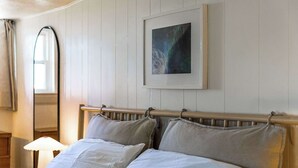 Hotellihuone, jossa on sänky, yöpöytä, lamppu, ikkuna ja seinällä oleva kehystetty kuva.