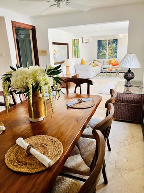 A dining area with a wooden table, woven placemats, and a vase of flowers. - Make Memories at Mango Crescent (Saint James)
