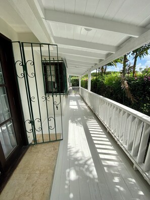 A covered corridor with white railings, a tiled floor, and a view of lush greenery outside. - Make Memories at Mango Crescent (Saint James)