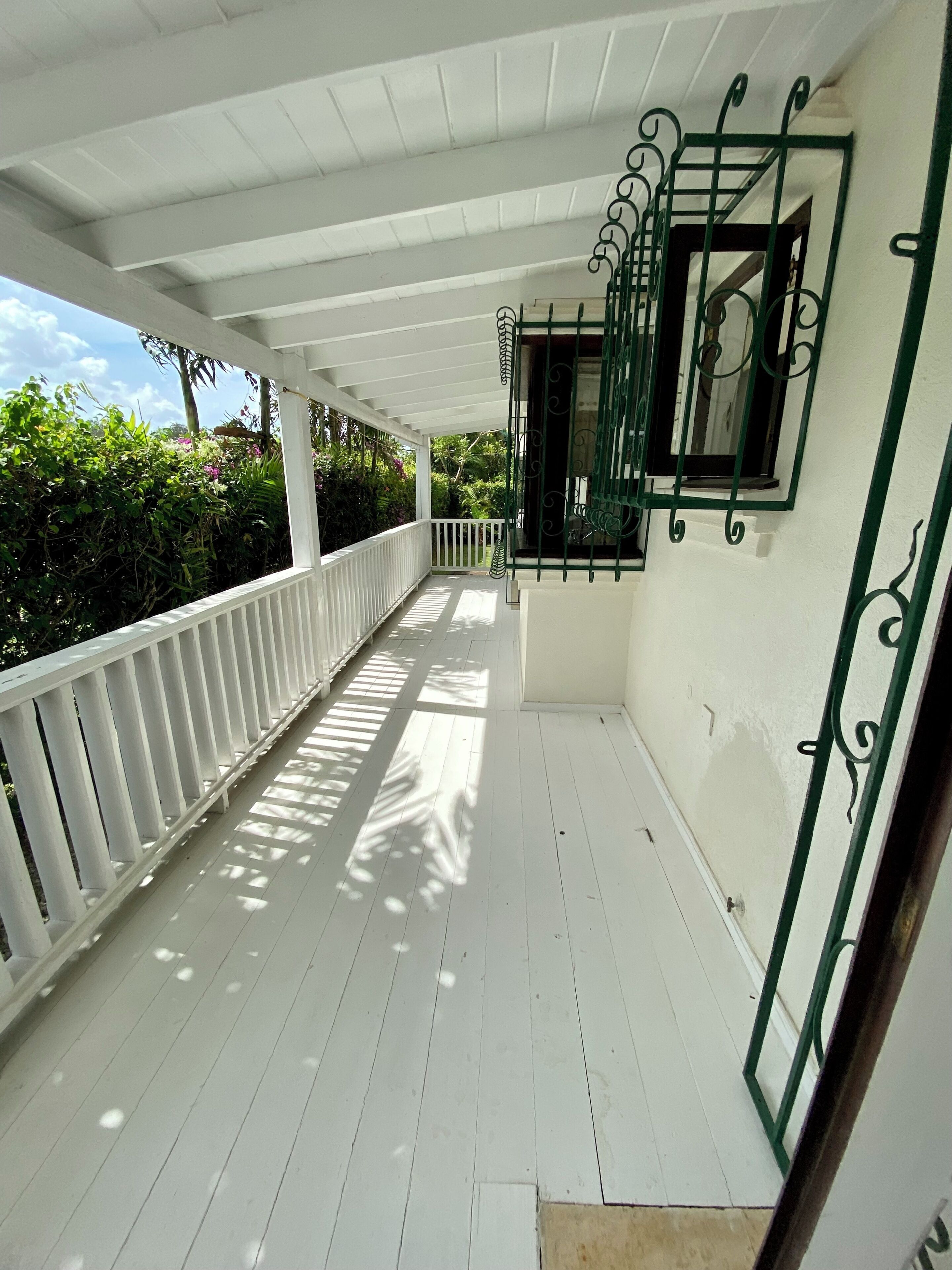 A covered porch with white railings and a green metal gate, leading to a white building with a window.