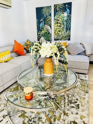 A living room with a glass coffee table, a sofa with cushions, a vase with flowers, and two paintings on the wall. - Make Memories at Mango Crescent (Saint James)