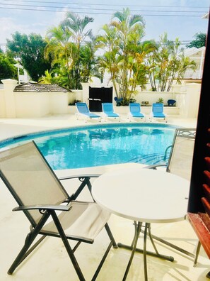 A swimming pool with lounge chairs and a table, surrounded by palm trees and a white building. - Make Memories at Mango Crescent (Saint James)