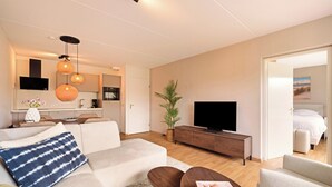 Una sala de estar moderna con sofá, mesa de centro, televisor y un comedor con mesa y sillas.