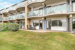 A multi-story residential building with balconies, a patio area with outdoor furniture, and a well-maintained lawn. - Seaside Retreat Apartment in Callantsoog (Callantsoog)