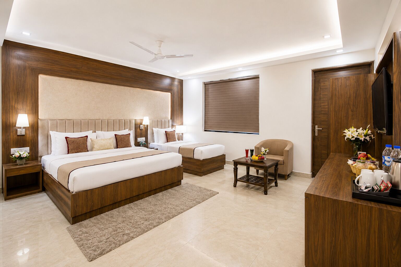 Quarto de hotel com uma cama grande, uma cama menor, uma escrivaninha com cadeira, televisão e ventoinha de teto.