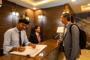 Una reception con un uomo che firma un documento, una donna dietro al bancone e un altro uomo che parla.
