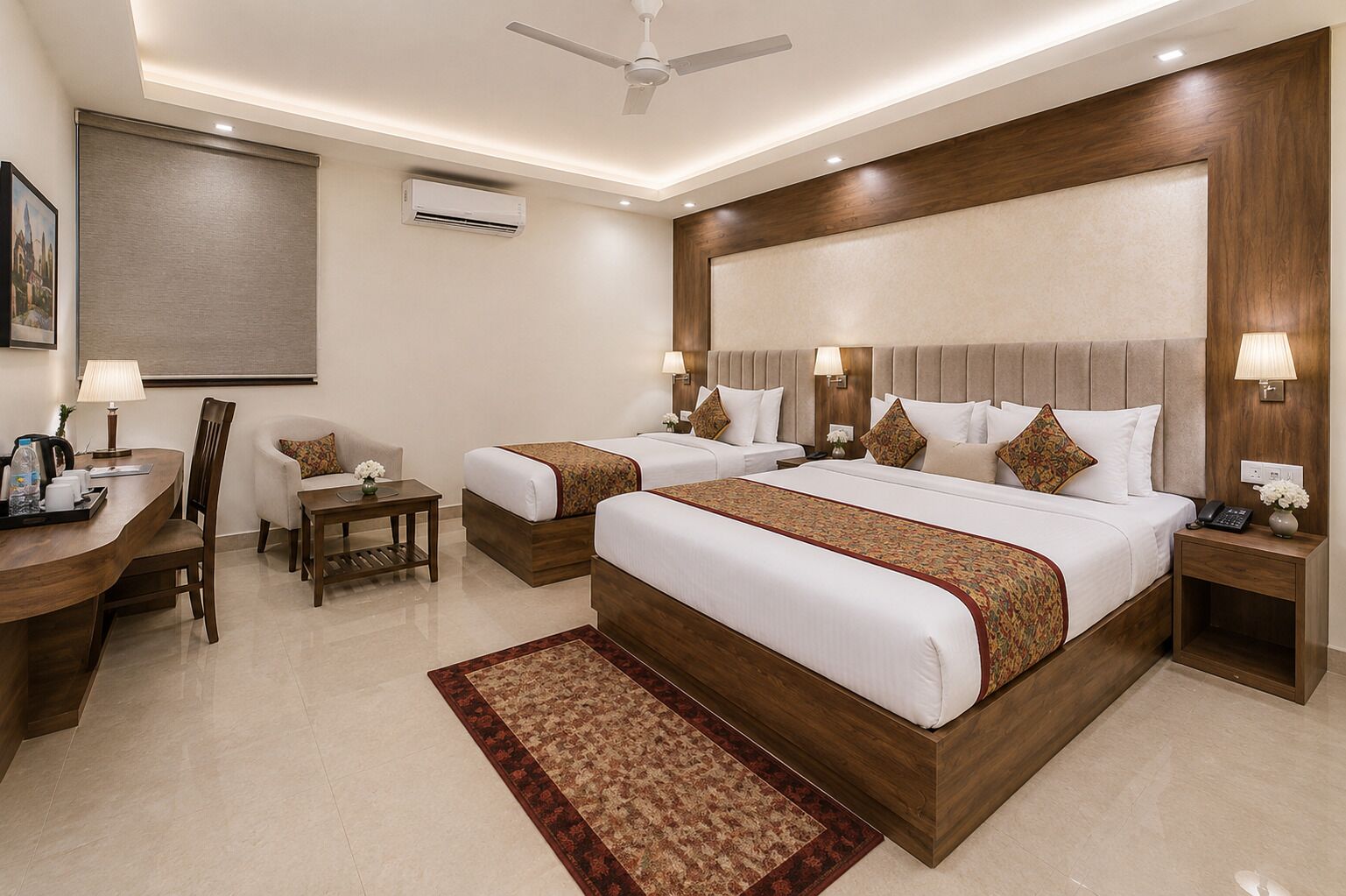 Habitación de hotel con dos camas, un escritorio, sillas, una mesita, una lámpara, aire acondicionado y ventilador de techo.