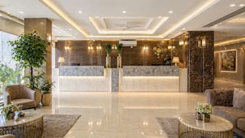 Vestíbulo de hotel con mostrador de recepción, zona de estar y plantas decorativas.