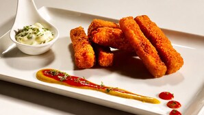 En hvid tallerken med paneret mad, en lille skål sauce og et dekorativt sausemønster.