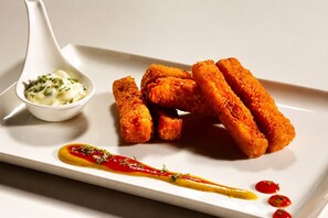 A white plate with breaded food items, a small bowl of sauce, and a decorative sauce line.