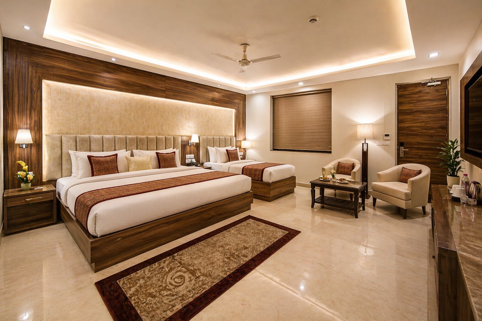 A modern hotel room with a large bed, a smaller bed, a seating area with a table, and a TV.