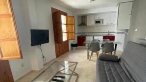 A living room with a glass coffee table, a grey sofa, and a kitchen in the background. - Castelo Silleria (Granada)