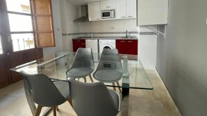 A modern kitchen with a glass dining table, grey chairs, white cabinets, and a red countertop. - Castelo Silleria (Granada)