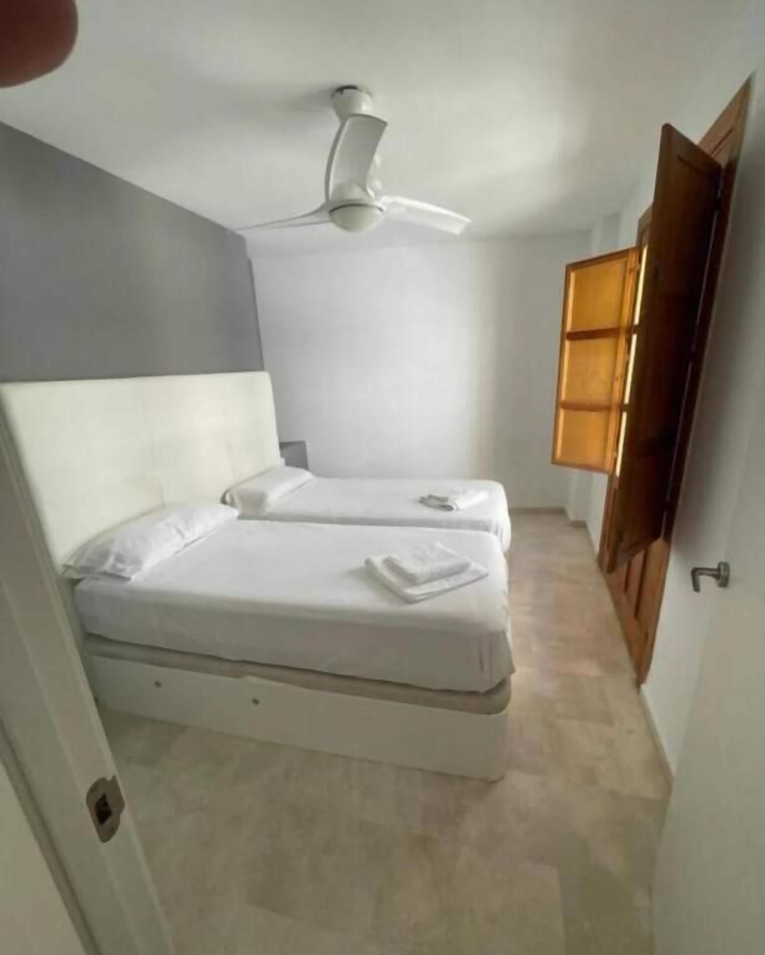 Un dormitori amb dos llits, un ventilador al sostre i una porta de fusta.