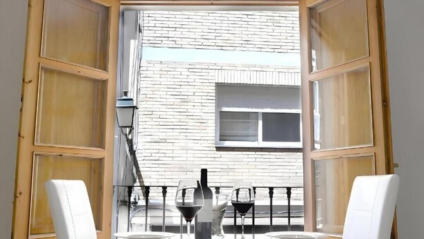 An open room with a dining table set for two, a bottle of wine, and a window with a view of a brick building. - Castelo Silleria (Granada)