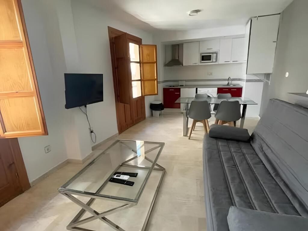 A modern living room with a glass coffee table, a grey sofa, and a TV mounted on the wall.
