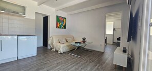 Une cuisine moderne avec des meubles blancs, un canapé beige, une table à manger en verre et une œuvre d’art colorée accrochée au mur.