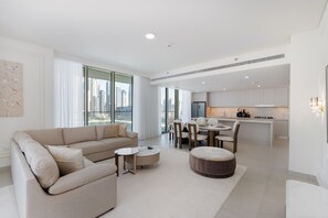 Ein modernes Wohnzimmer mit Sofa, Hocker und Couchtisch, ein Essbereich mit Stühlen und eine Küche mit Esstisch und Stühlen.
